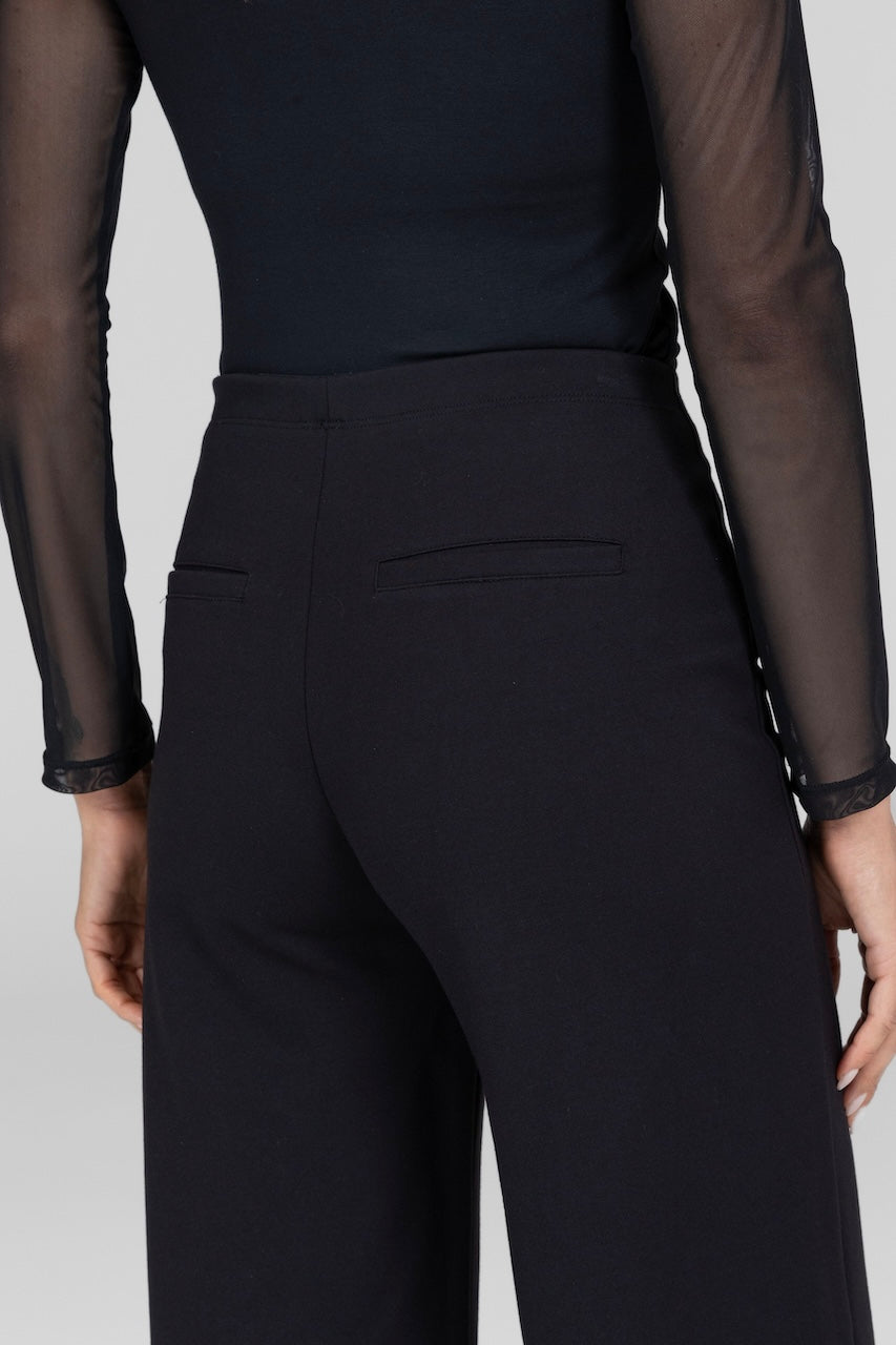 Close up of back of model wearing long sleeve mesh top with black high waist with pockets on the back