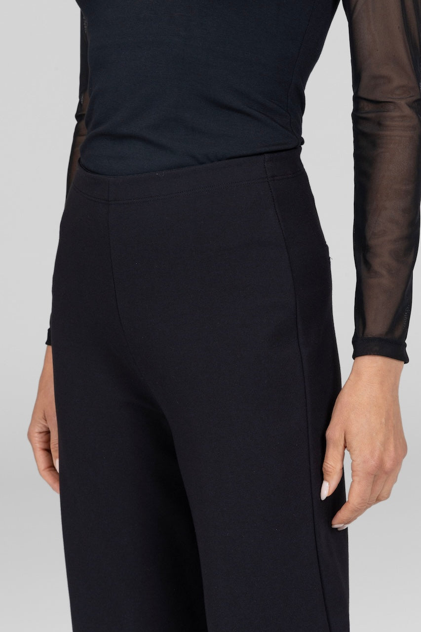 Close up shot of model from waist to knee wearing black mesh long sleeve top and black high waisted pants