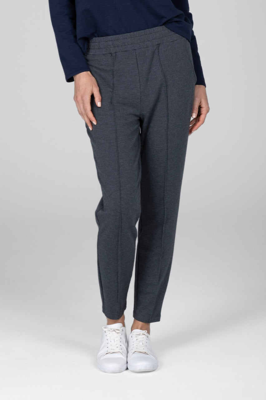 A woman wearing charcoal heather gray pintuck joggers and a navy top, standing against a plain background.