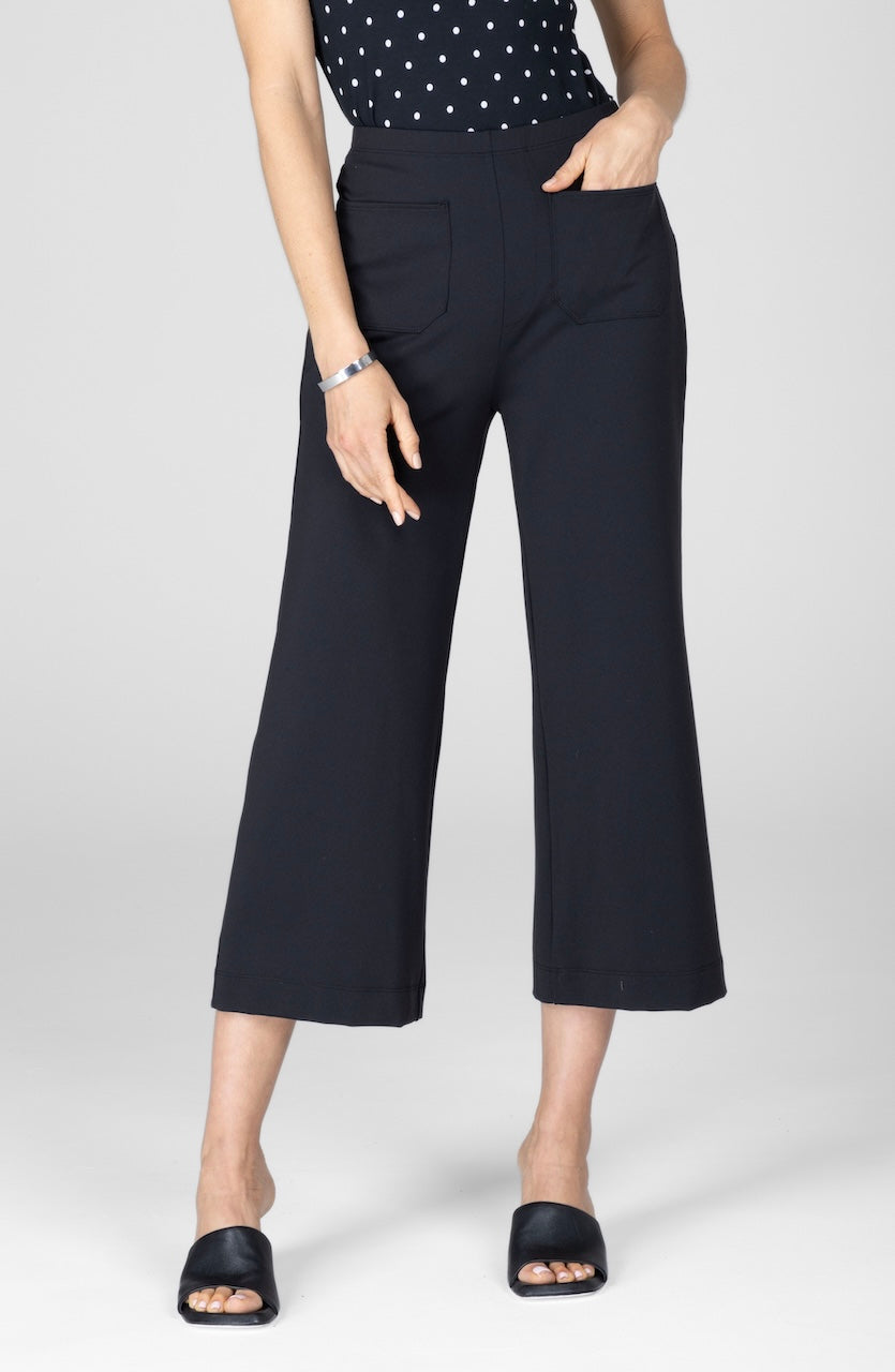 A person wearing high-waisted black crop pants with front patch pockets and a polka dot top.