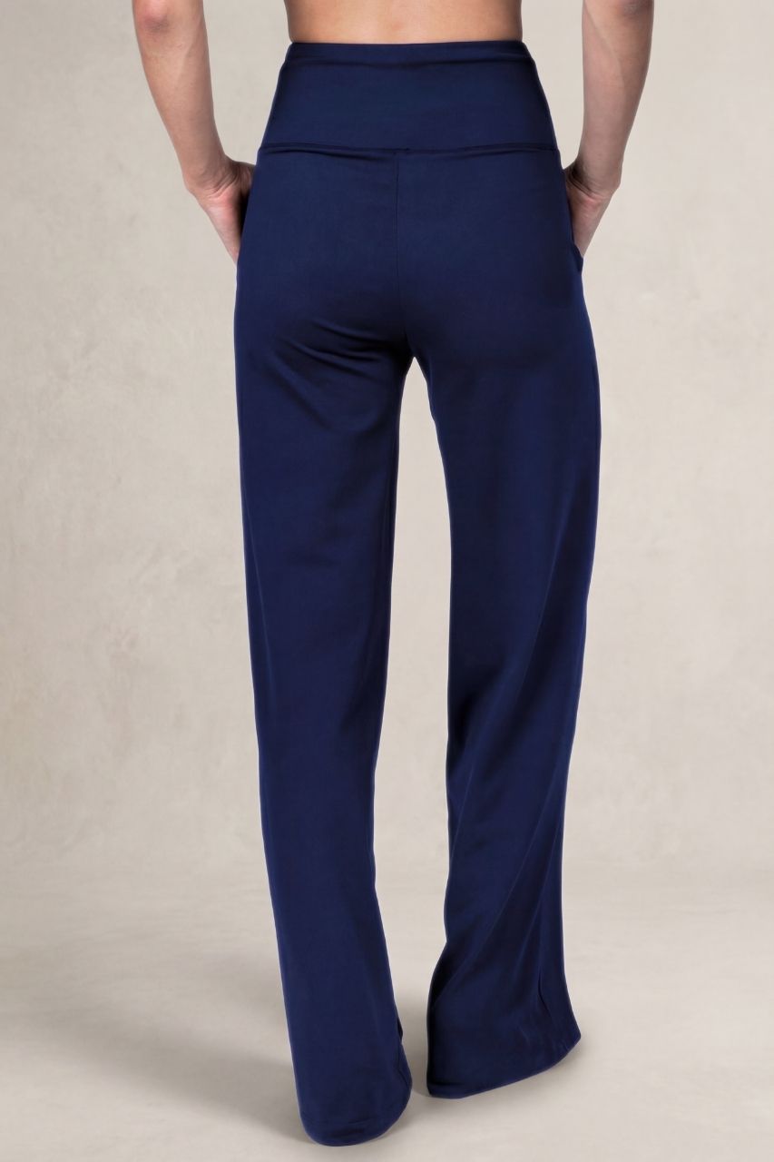 Back view of a woman wearing navy blue high waisted pants in front of a beige background