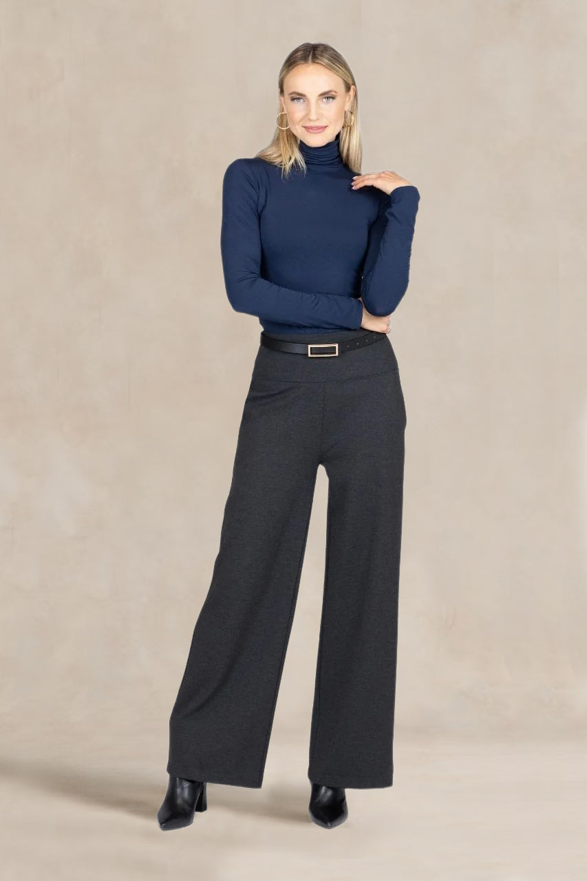 Woman wearing a navy turtleneck and gray wide-leg pants on a beige background