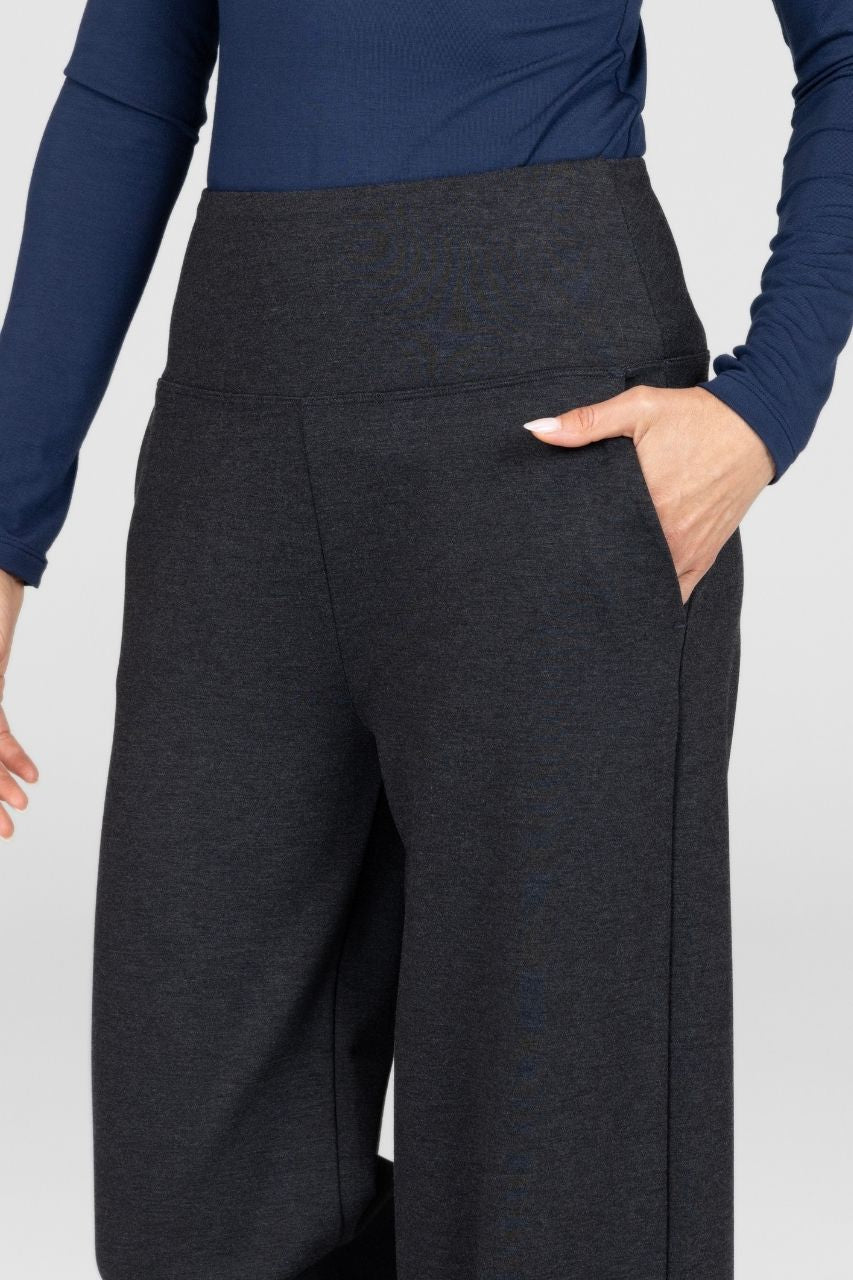 Close up of a woman wearing dark gray wide-leg pants with a blue top on a white background