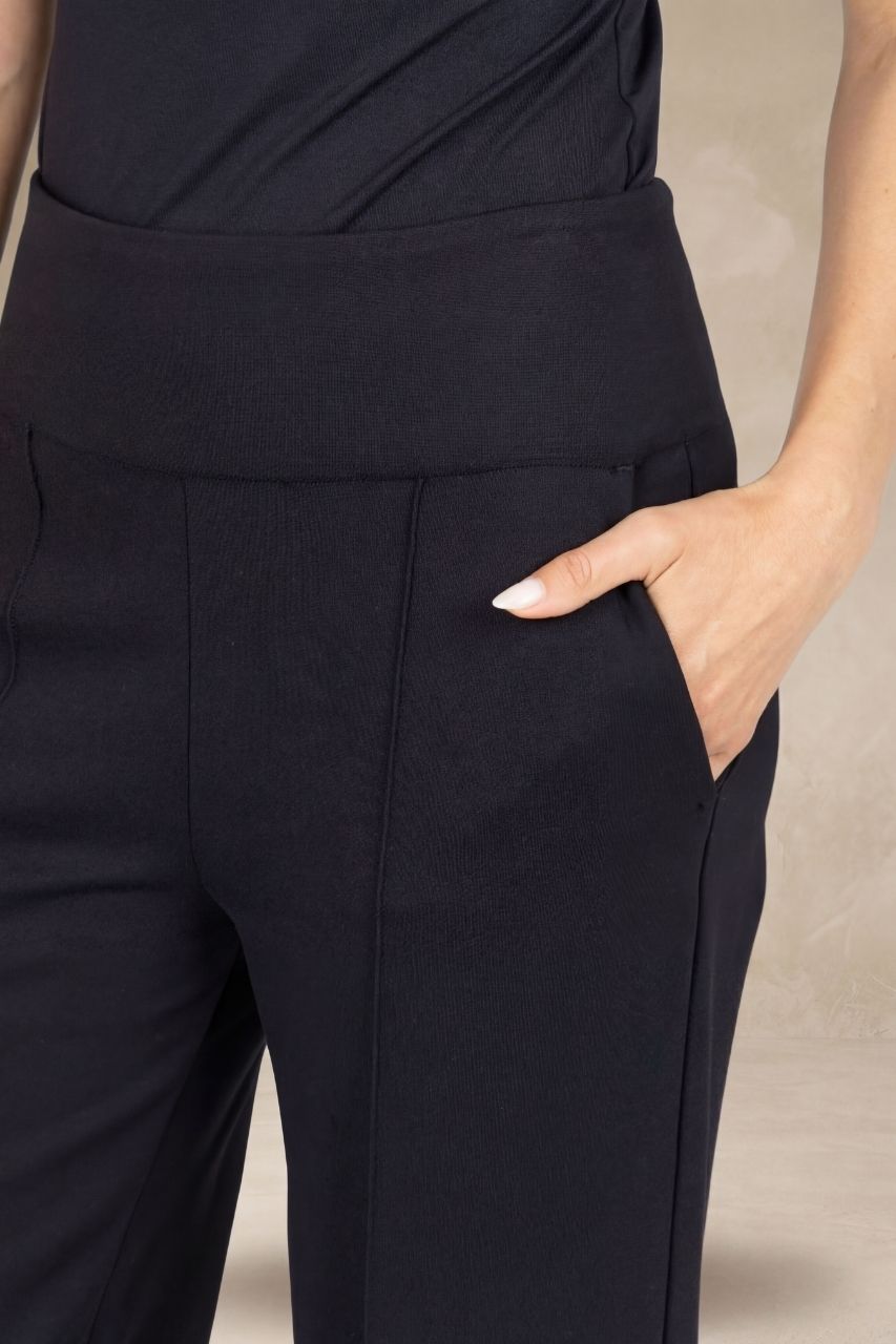 Close up view of black pants on a model in front of a beige background