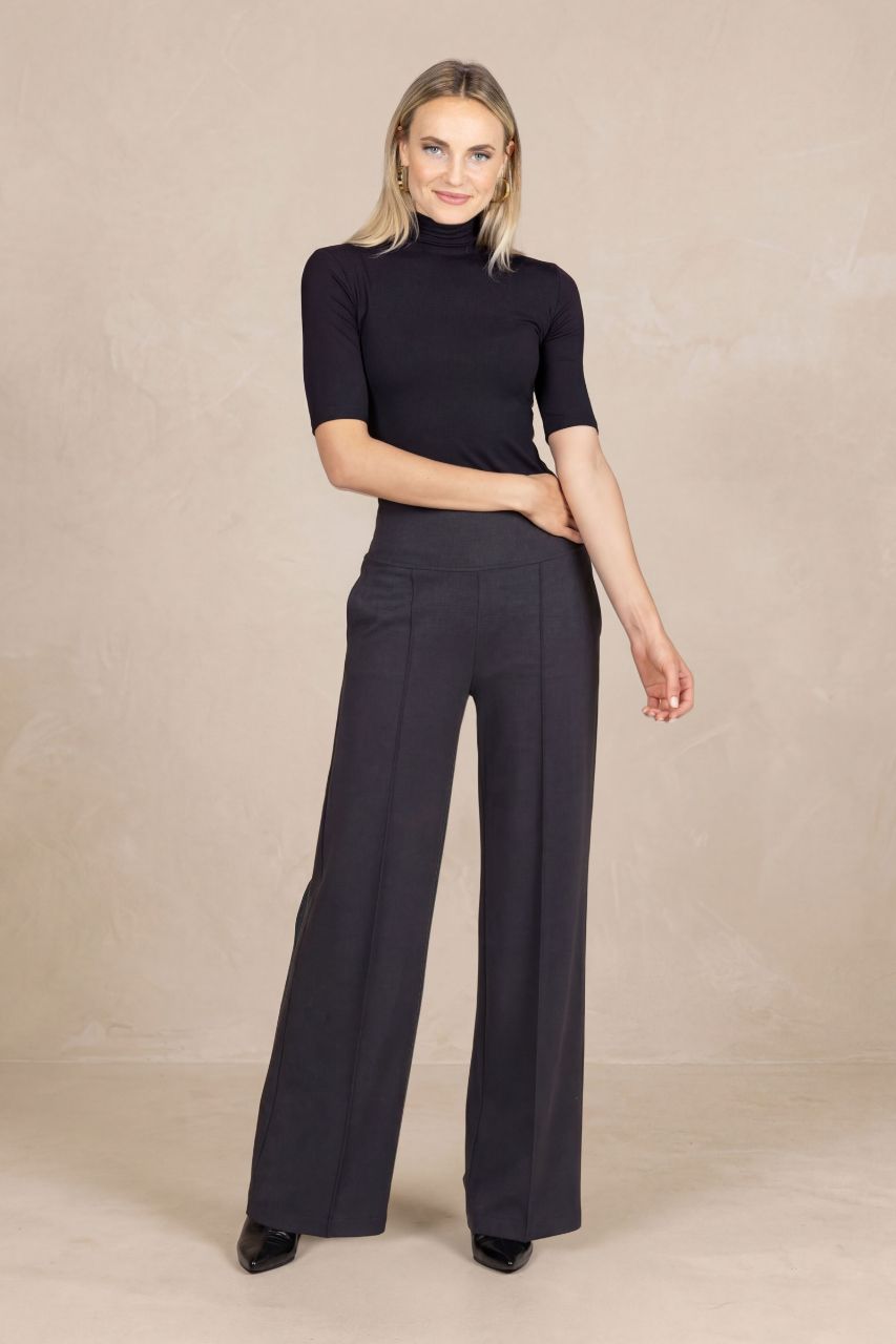 Woman wearing a black short sleeve mock neck and charcoal wide-leg pants on a beige background