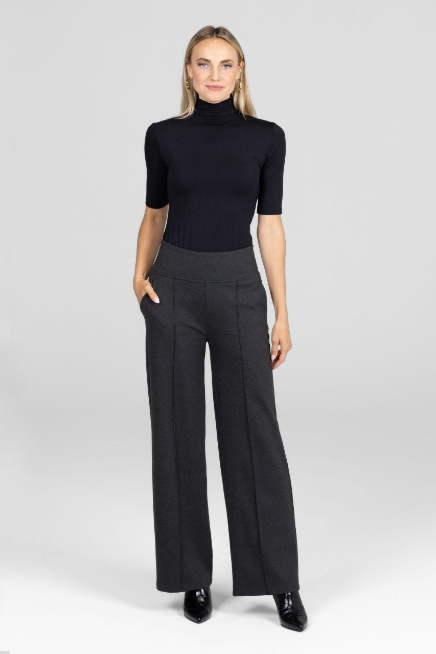 Woman wearing a black mock neck and gray wide-leg pants with pintucks on a white background