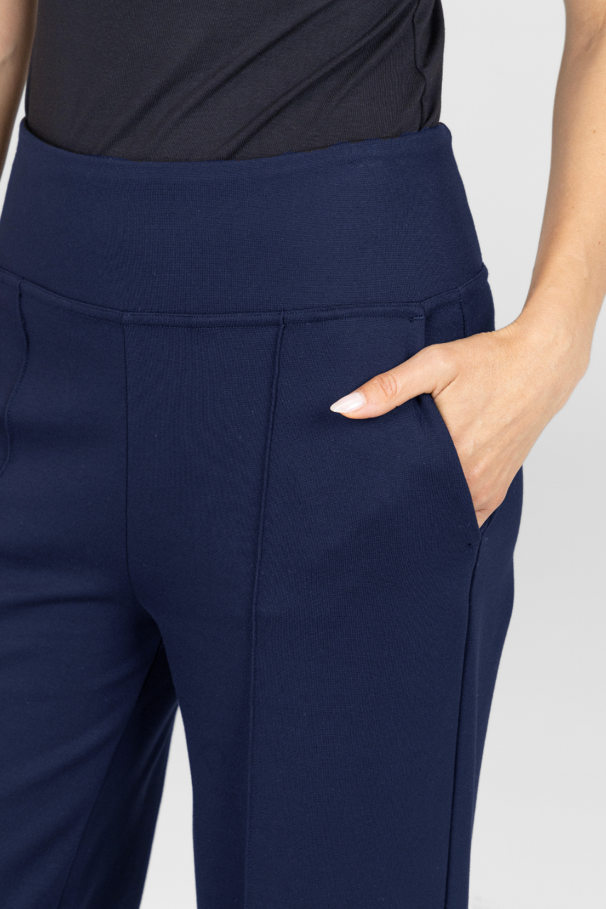 Close up view of navy blue pants with front pintucks worn by a woman on a light gray background