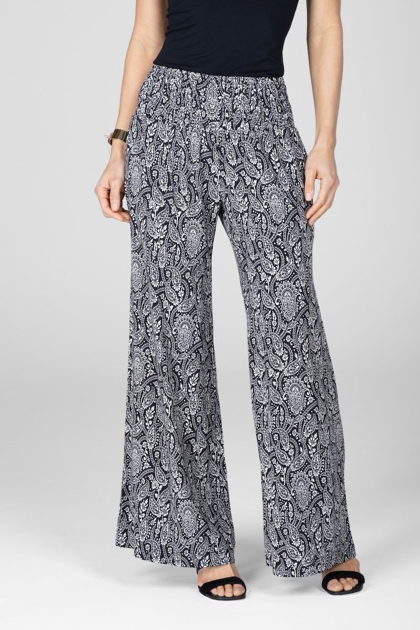 A woman wearing wide-leg black paisley print pants with a smocked waistband and side pockets.