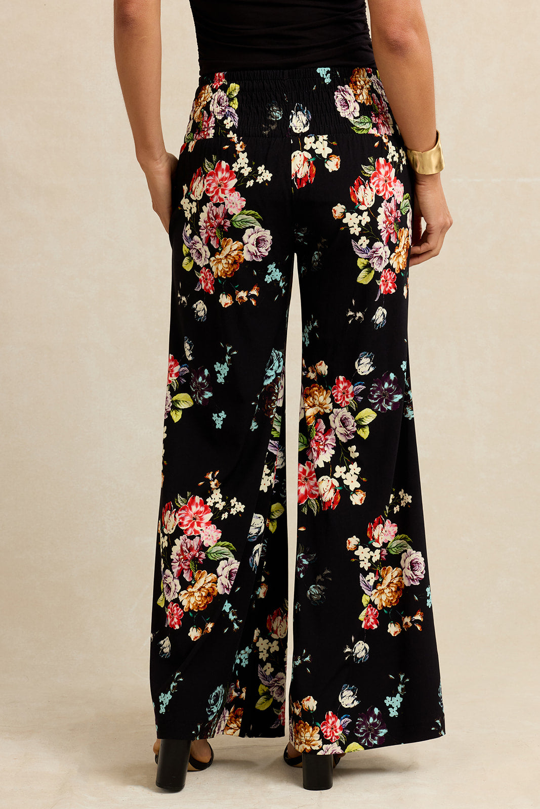 Black wide-leg pants with colorful floral patterns worn by a person on a beige background