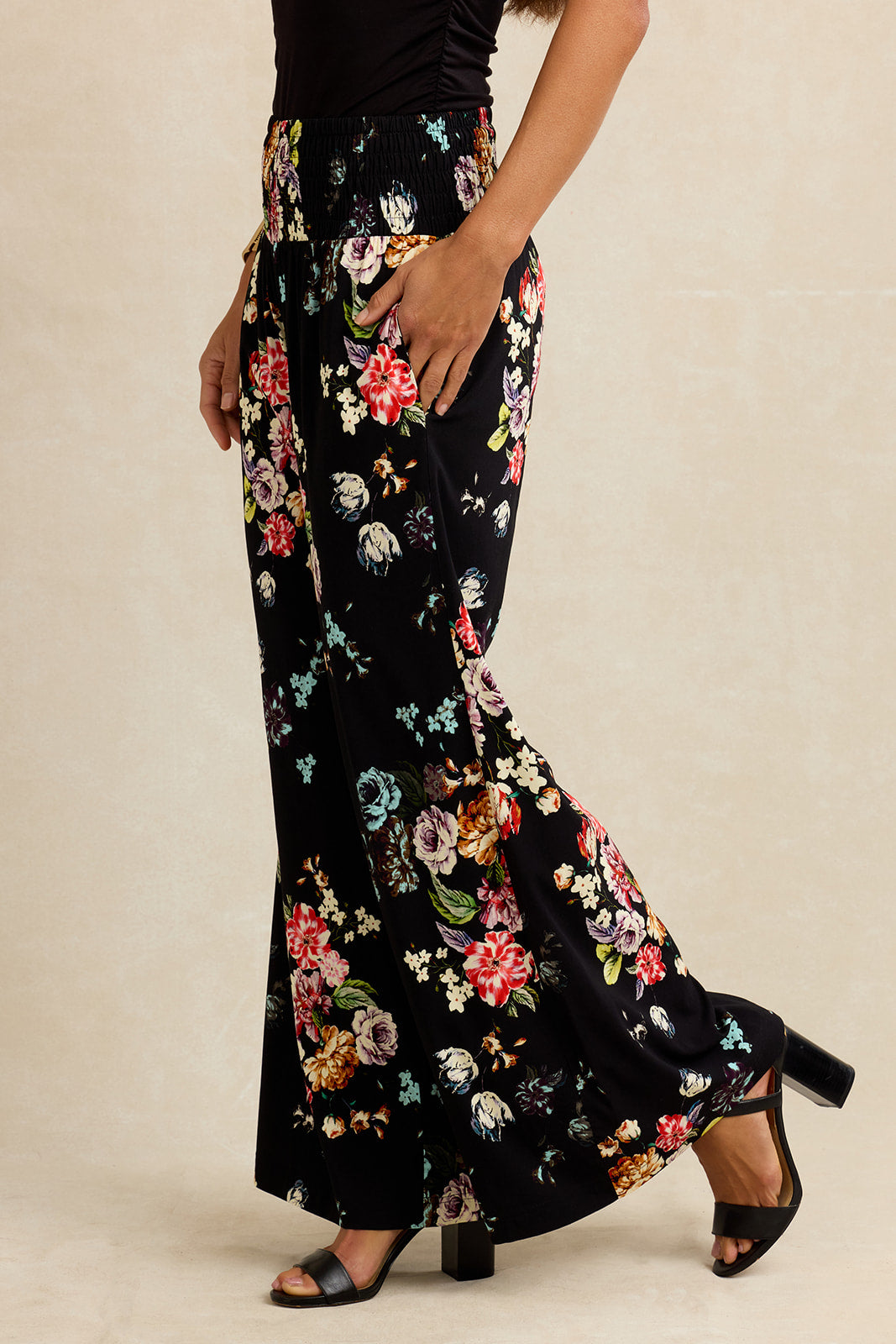 Floral-patterned black pants worn by a person on a beige background