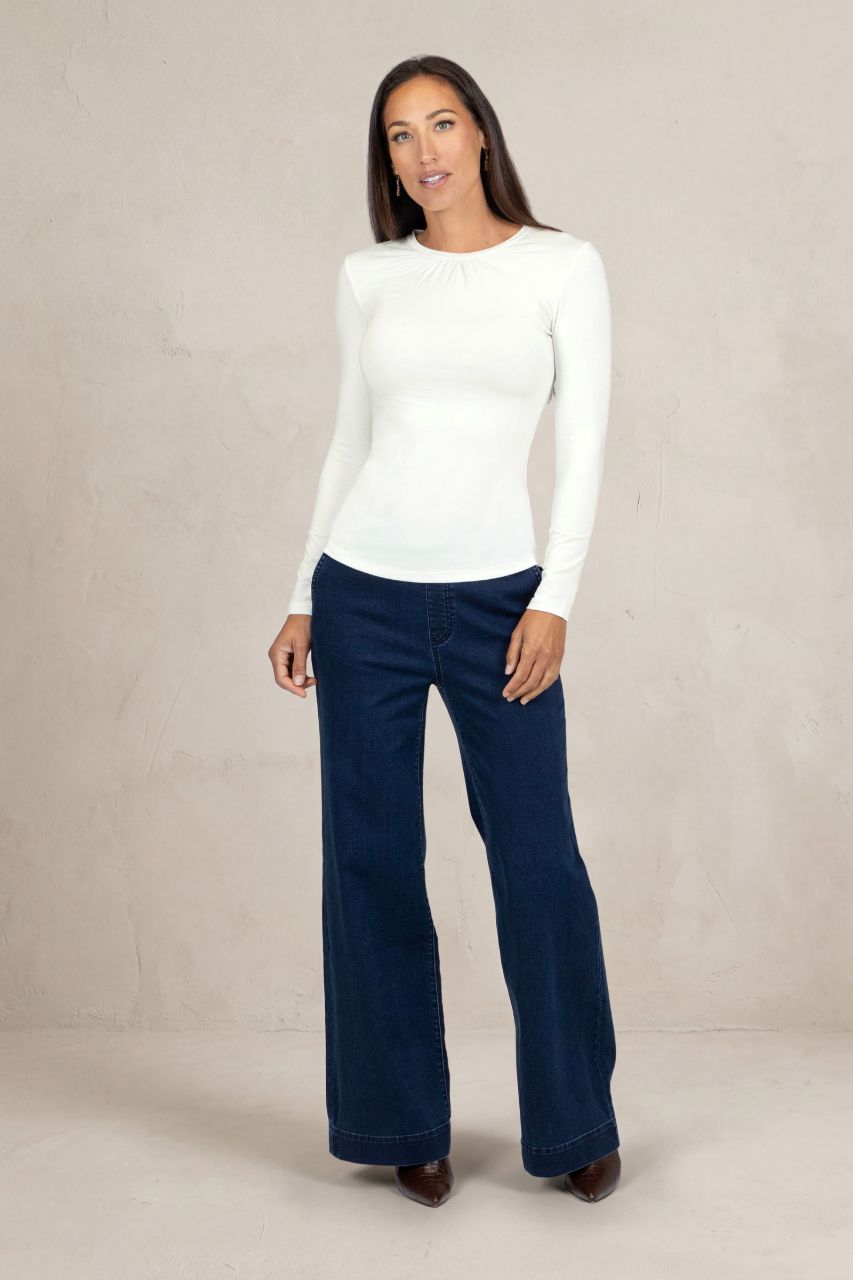 Woman wearing a white sweater and navy denim pants against a beige background