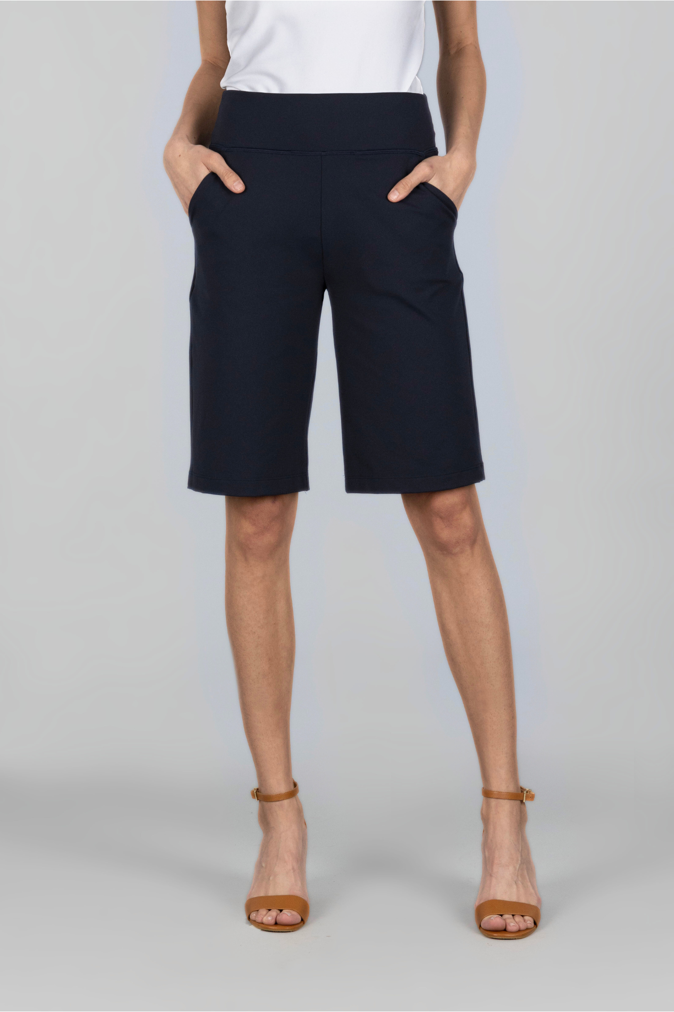 Female model wearing a white shirt and black knee length shorts with hands in her pockets