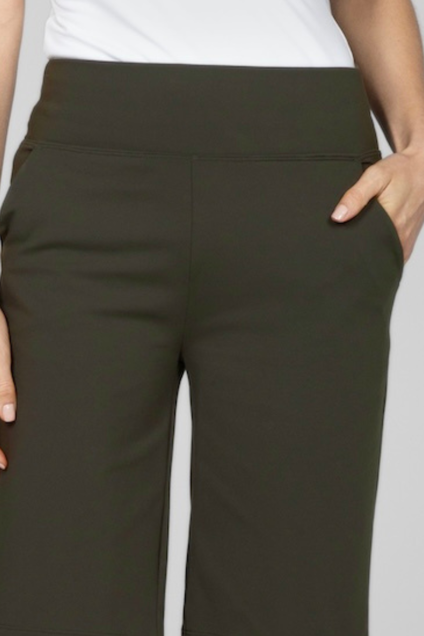 Close up photo of a woman's waist down to knee wearing a white tank and knee length dark green bermuda shorts. One hand in front pocket.