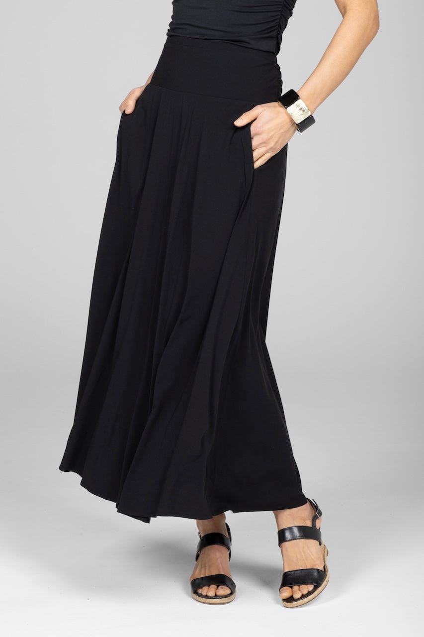A model wearing a black maxi skirt with a flowy silhouette, standing against a plain background.