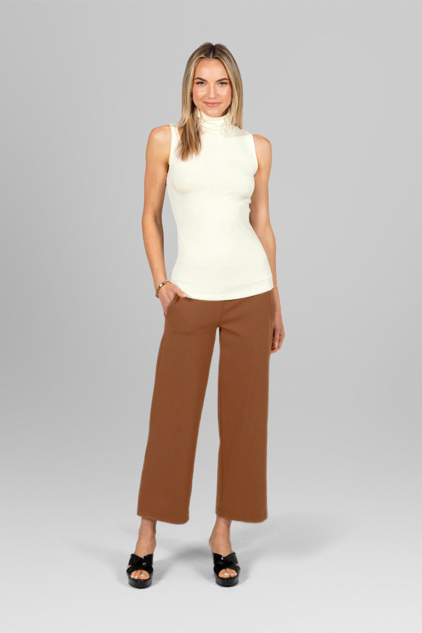 Woman wearing a sleeveless ivory turtleneck and dark khaki wide-leg ankle pants.