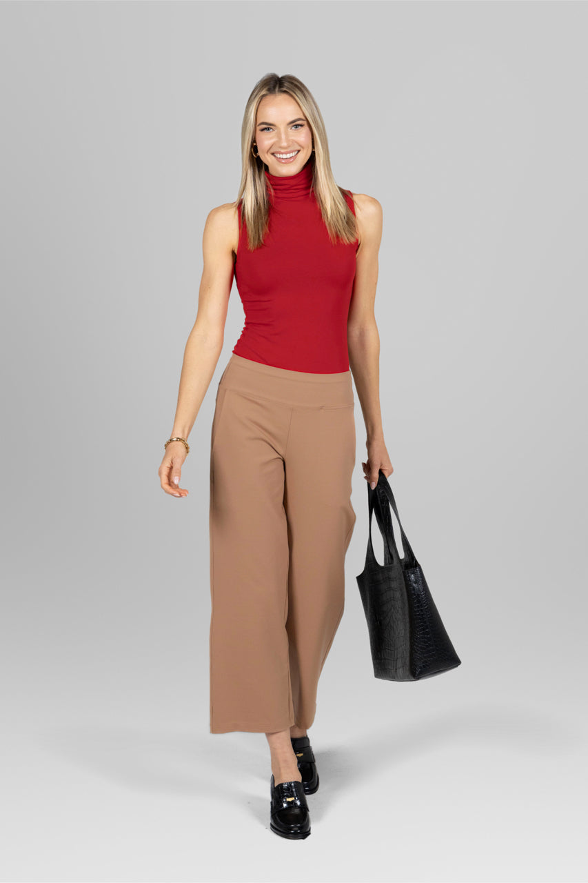 Woman wearing a red top and holding a purse, styled with the Traveler Ankle Pant in khaki, creating a chic and professional look perfect for the workplace