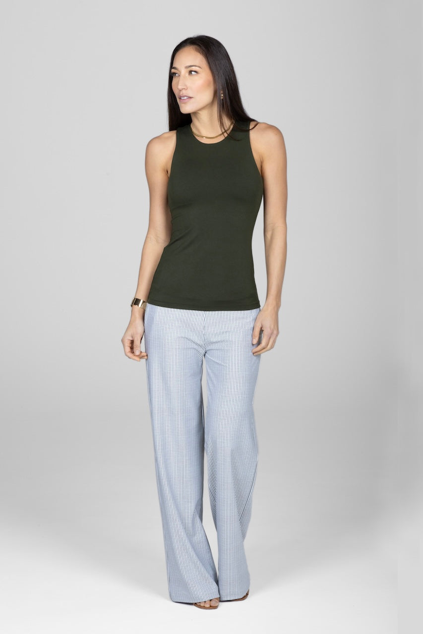 A woman standing, wearing a forest green sleeveless tank top and striped wide leg pants.