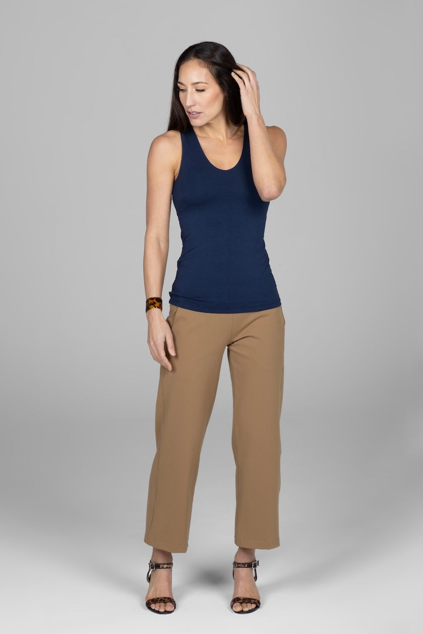 A woman wearing a navy blue sleeveless top and beige trousers, standing against a grey background.