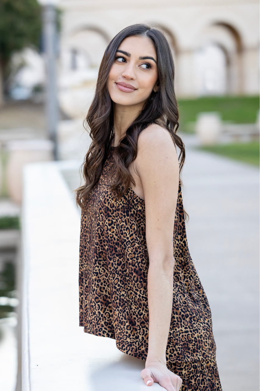 Woman leaning over white rail wearing a full leopard print top and bottom, worn as a set