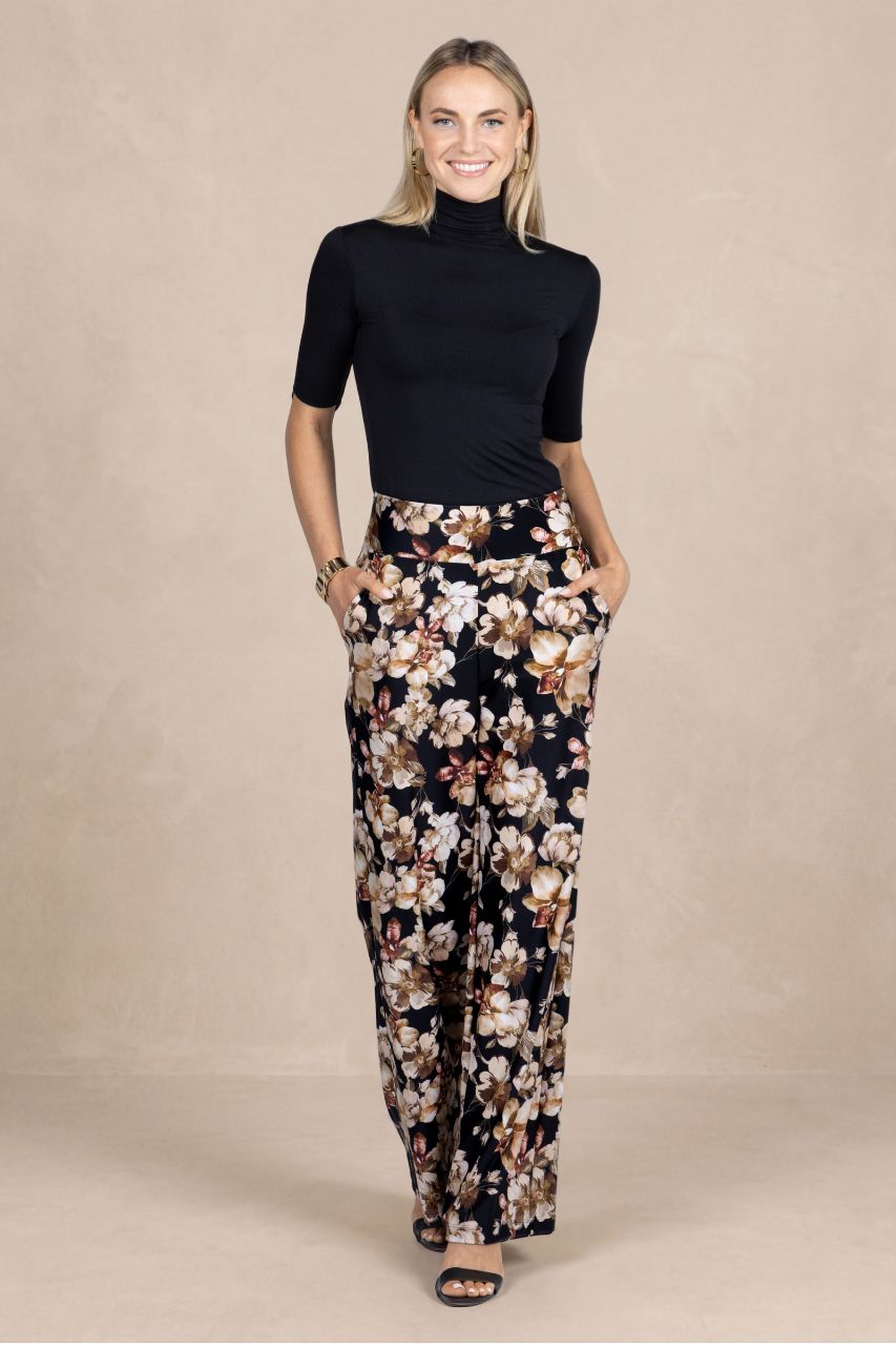 Woman wearing a black mockneck and floral pants on a beige background