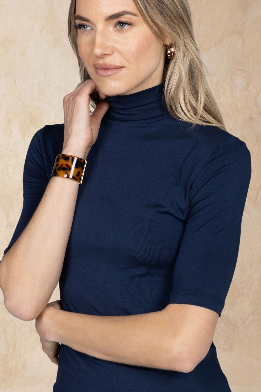 Woman wearing a navy mockneck shirt against a beige background