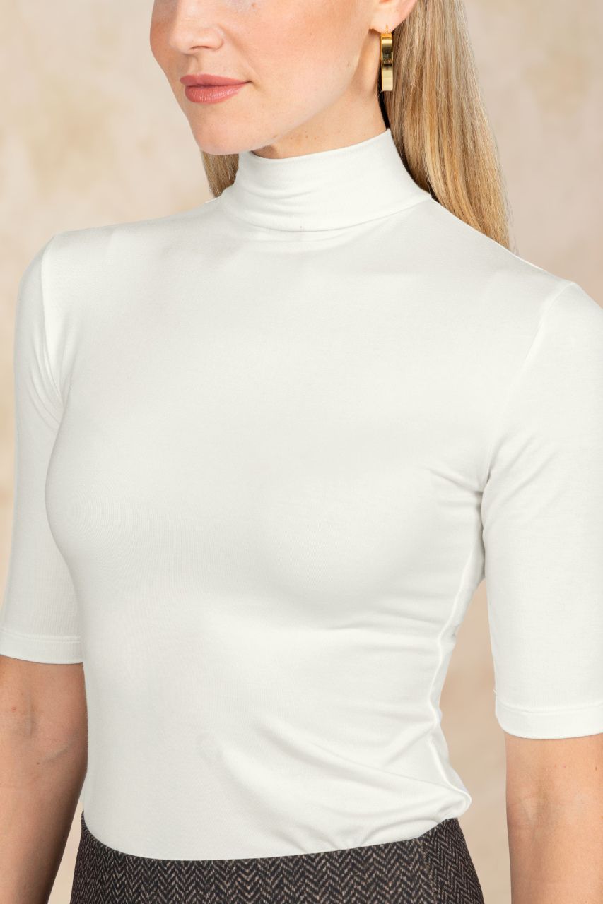 Woman wearing an ivory mockneck top against a beige background