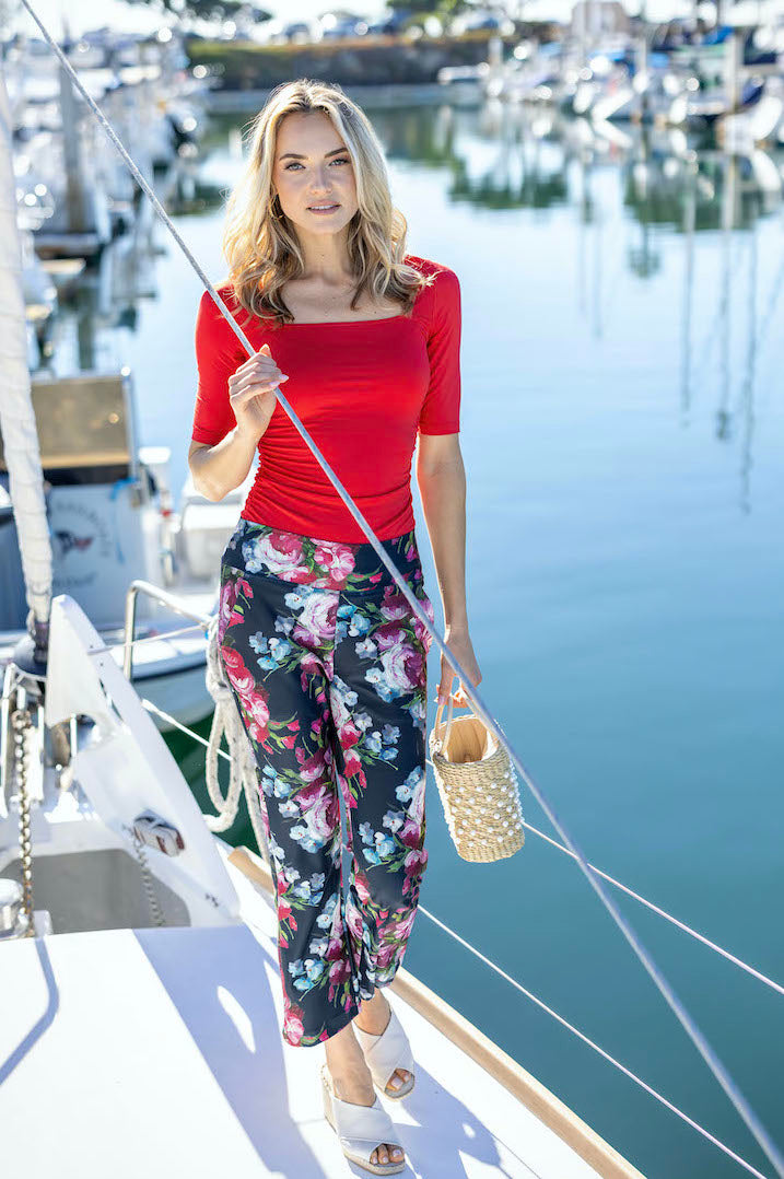 Woman on a boat wearing a red top paired with the High Waist Ankle Kick Pant in spring floral, showcasing a fun and vibrant outfit perfect for a day on the water