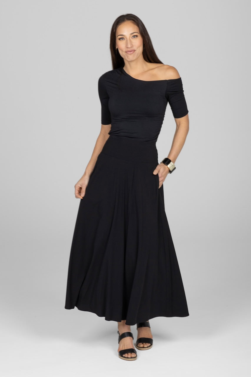Full length photo of a woman wearing black one shoulder short sleeve top with a black maxi skirt.