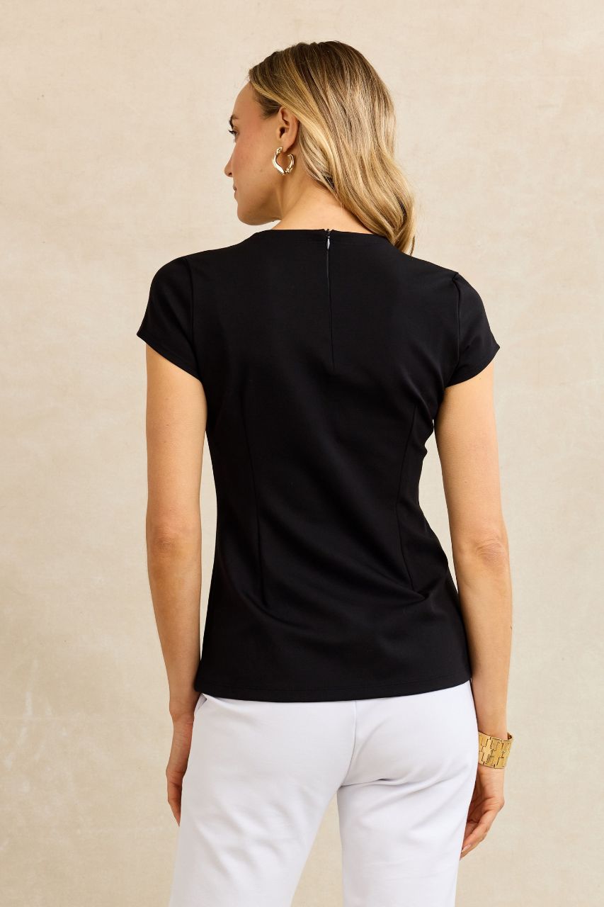 Back view of a woman wearing a black top and white pants against a beige background