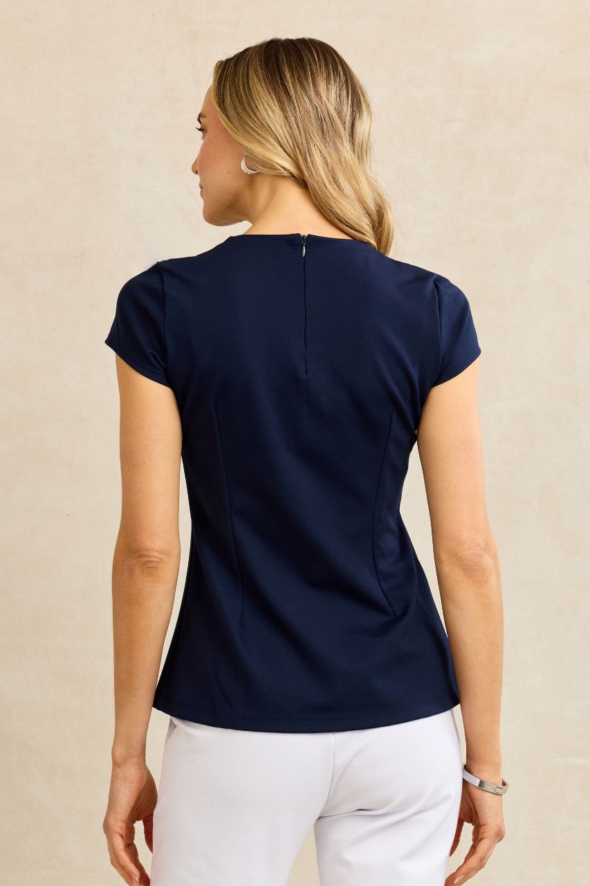 Back view of woman wearing a navy blue top and white pants on a beige background