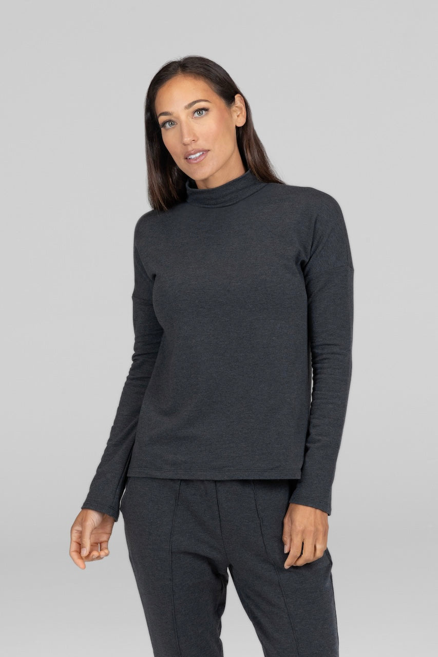 A woman wearing a long-sleeved charcoal heather mock neck top with matching sweatpants.