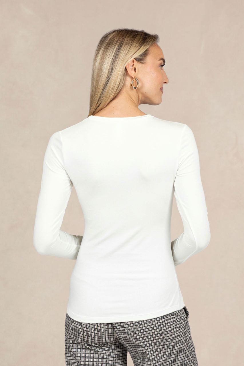 Woman wearing a white long-sleeve top and plaid pants against a beige background