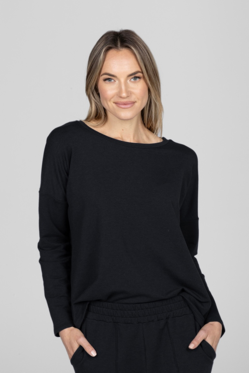 Woman wearing a black long sleeve top with both hands in the front pants pockets