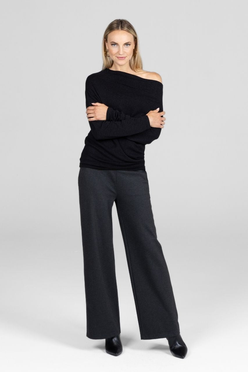 Woman wearing a black off-shoulder top and charcoal wide leg pants on a white background