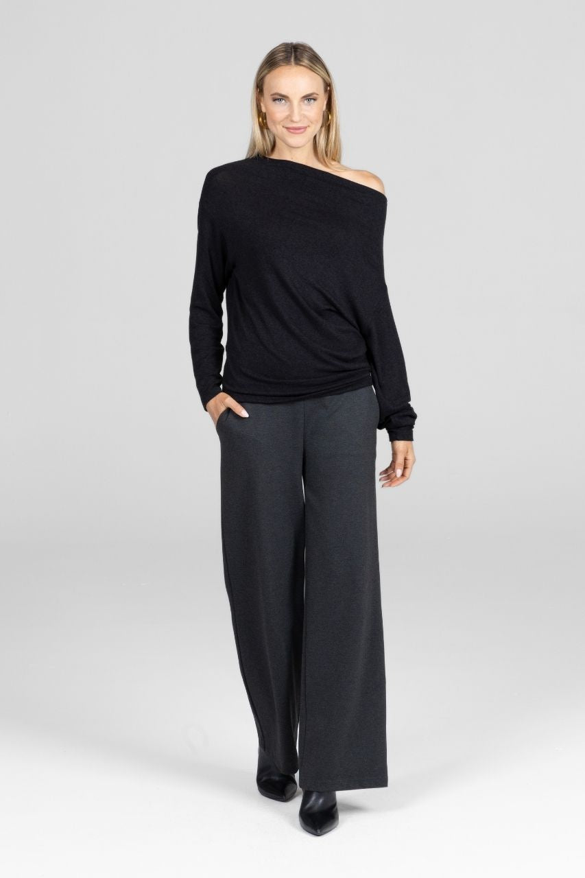 Woman wearing a black one-shoulder sweater and gray wide leg pants on a white background