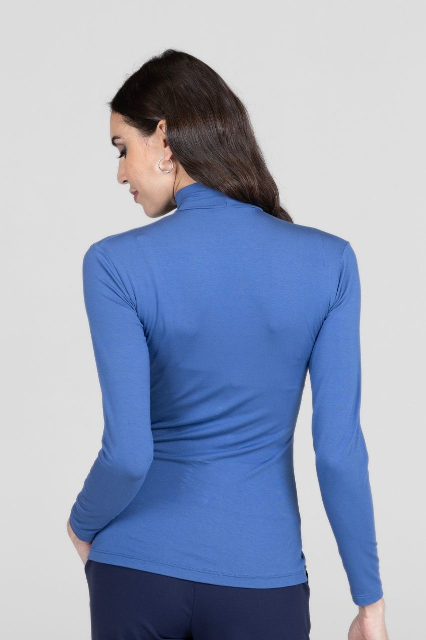 Back view of a woman wearing a blue long-sleeve mock neck top against a light gray background
