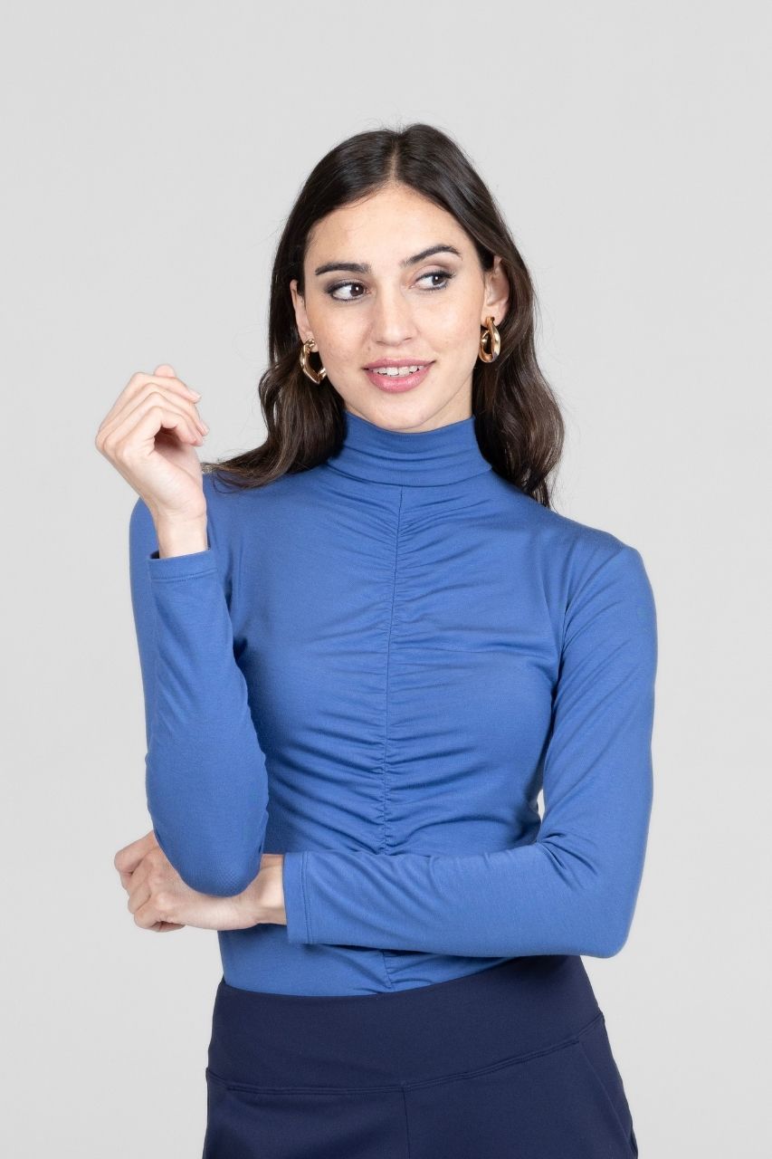 Woman wearing a blue mock neck shirt against a plain background