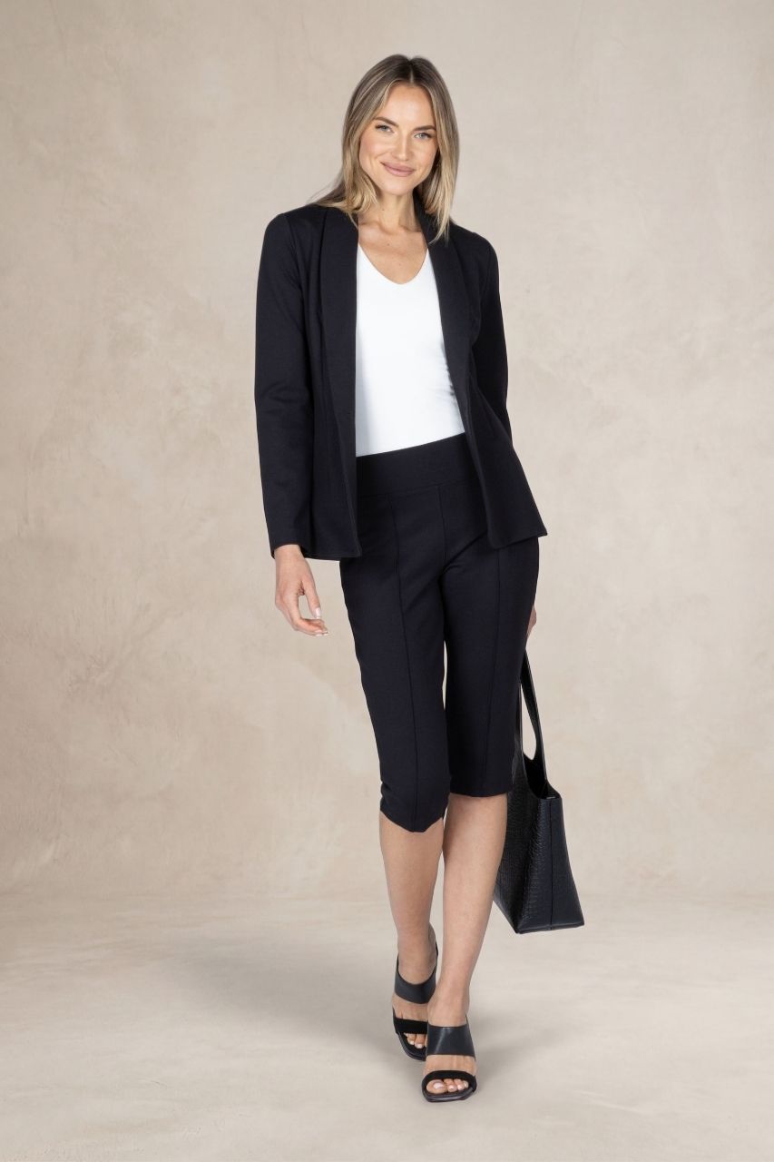 Full length image of a woman wearing a matching black outfit in front of a beige background