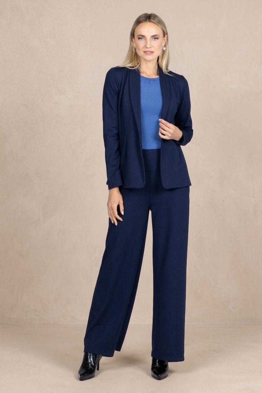 Full length image of a woman wearing a navy blue blazer suit in front of a beige background