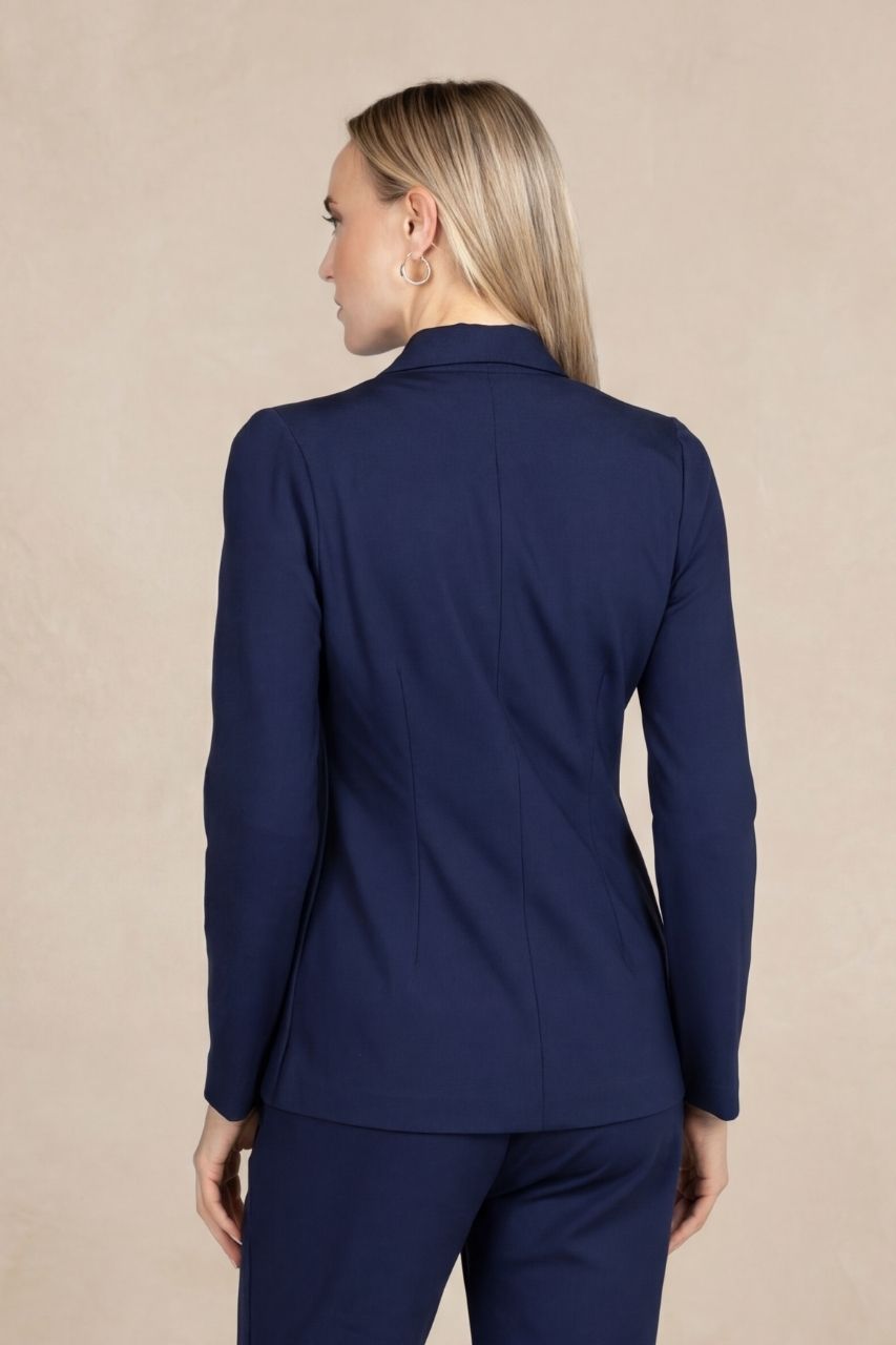 Back view of a woman wearing a matching navy blue pant suit in front of a beige background