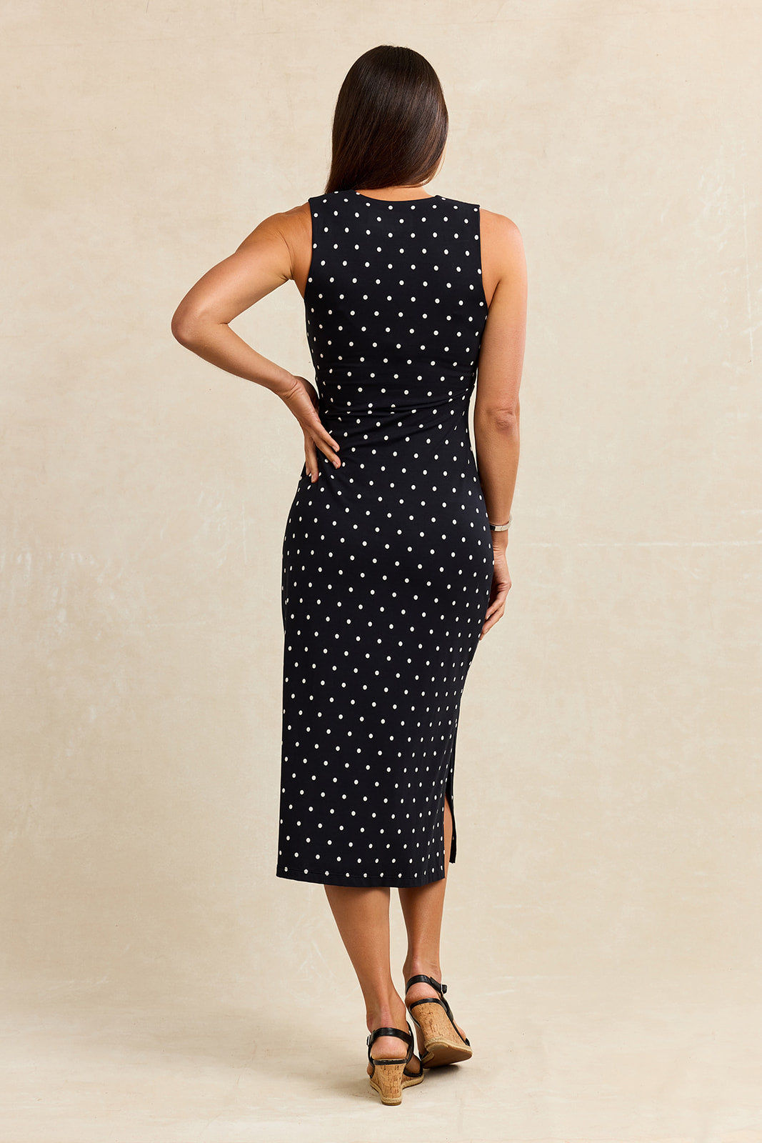 Back view of a woman wearing a black dress with white polka dots against a beige background