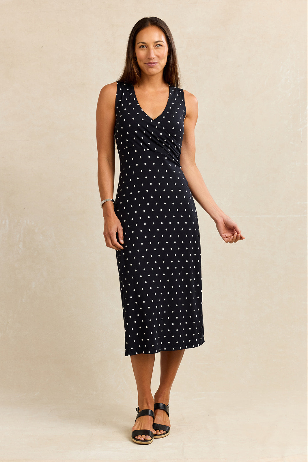 Woman wearing a black sleeveless wrap dress with white polka dots against a beige background