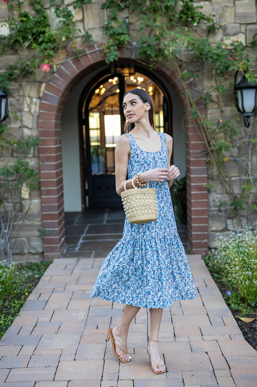 Model outside a garden building in JULIETTE MIDI DRESS: COTTAGE GARDEN holding a purse 