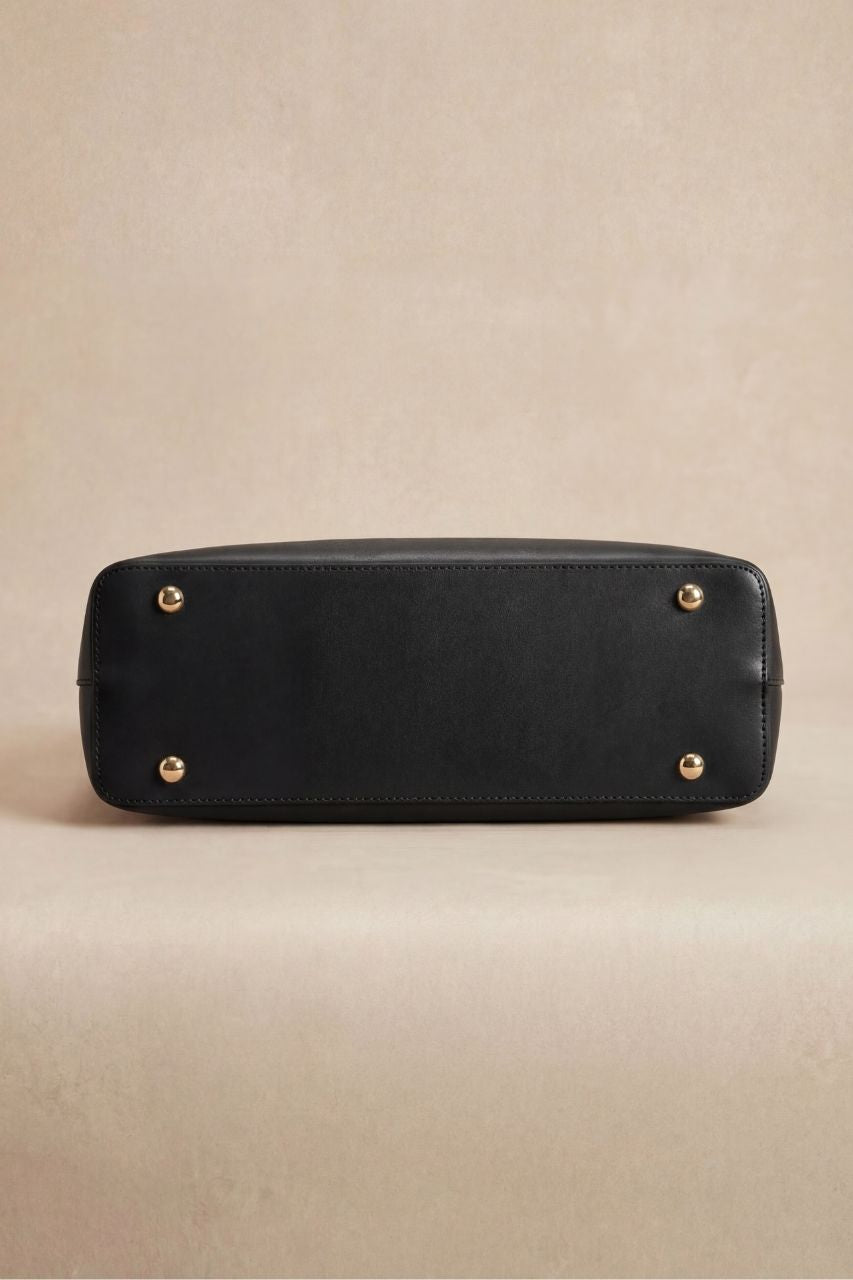 Black handbag with gold studs on the bottom on a beige background