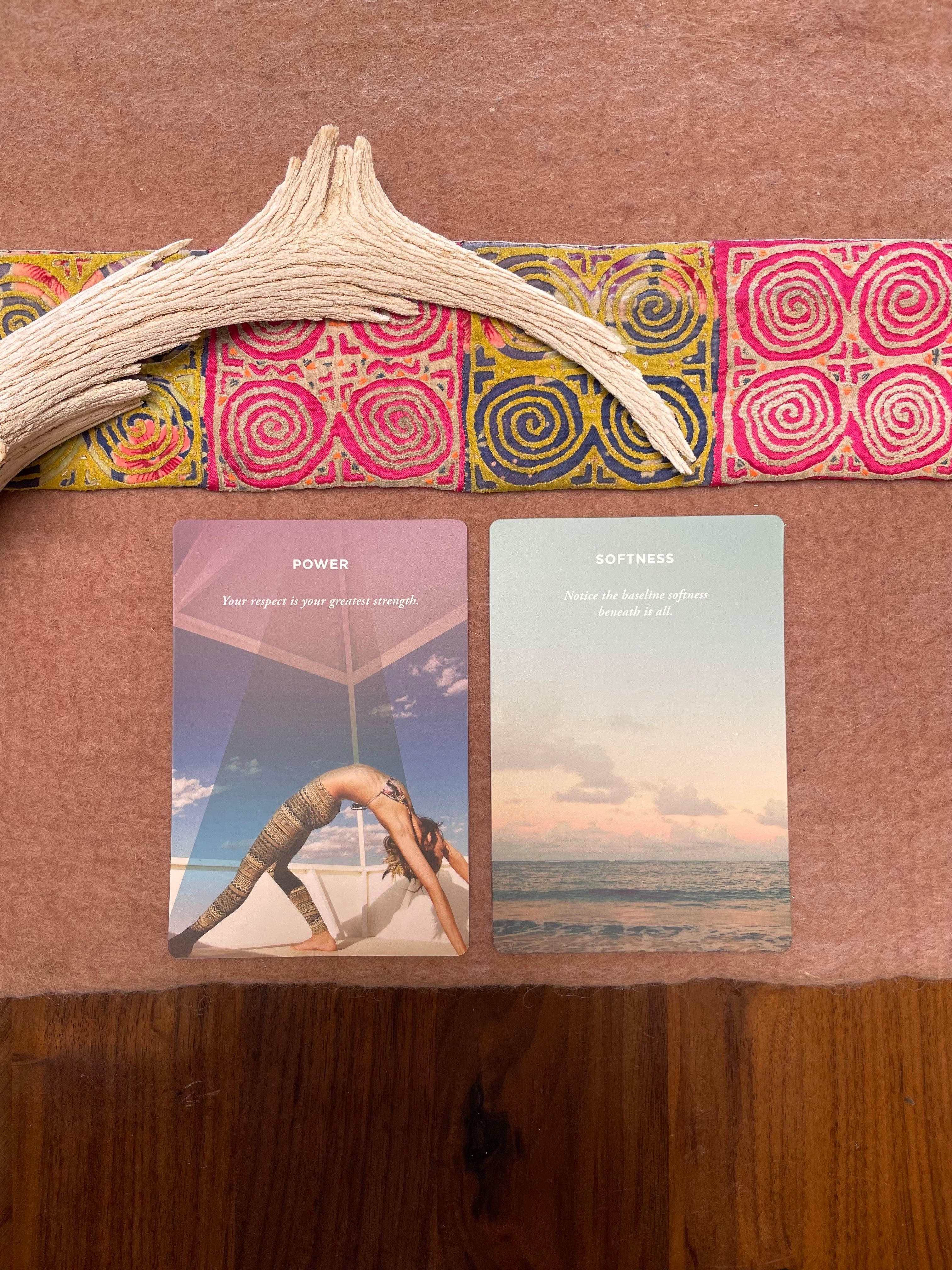 Two yoga cards on a wooden surface with a colorful fabric strip and natural object.