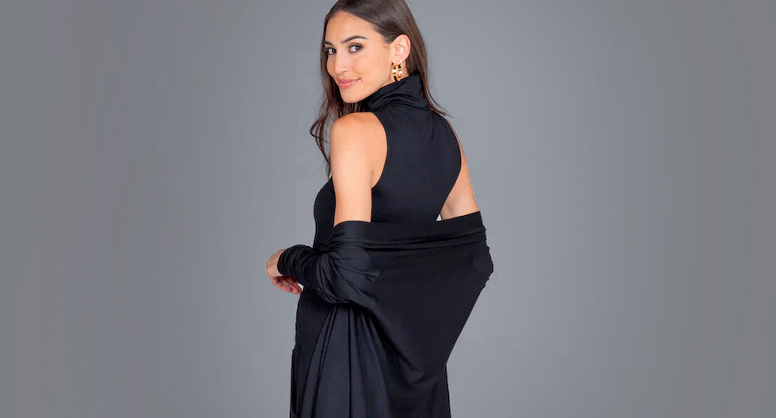 Woman looking over shoulder in black sleeveless turtleneck and cardigan. 