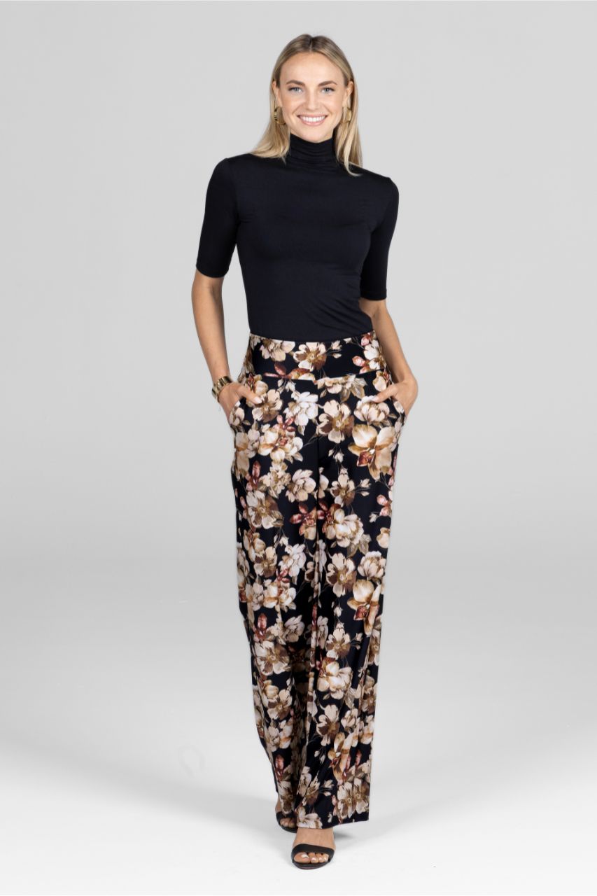 Woman wearing a black mockneck tee and floral wide leg pants on a white background