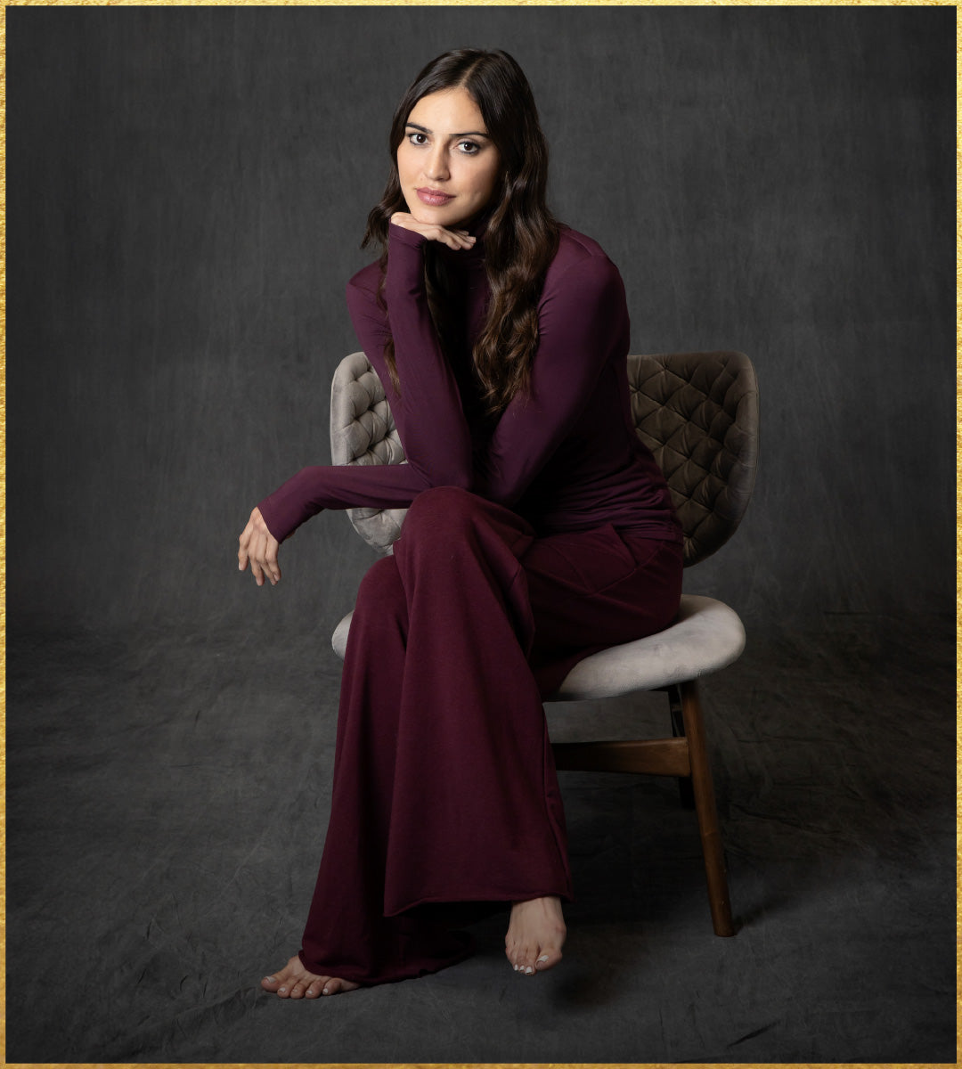 Woman in a burgundy outfit sitting on a chair against a dark background