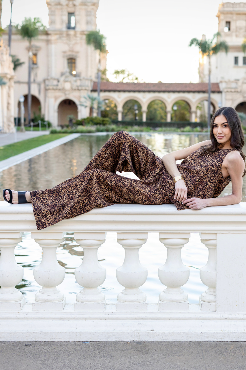 A woman sitting on a bench wearing a leopard print matching set with wide leg pants and black Heels.
