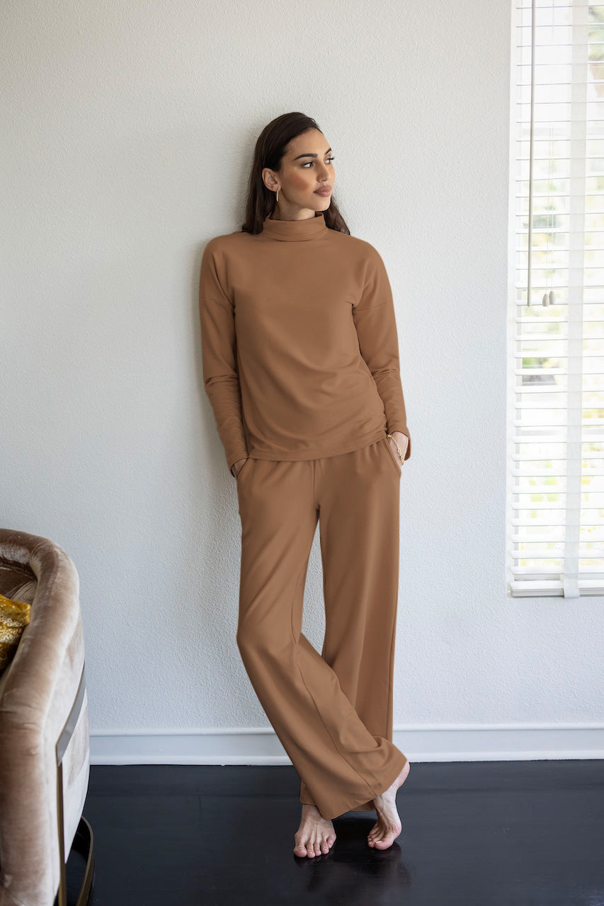 A woman standing in a room wearing a beige mockneck long-sleeved top and matching pants.
